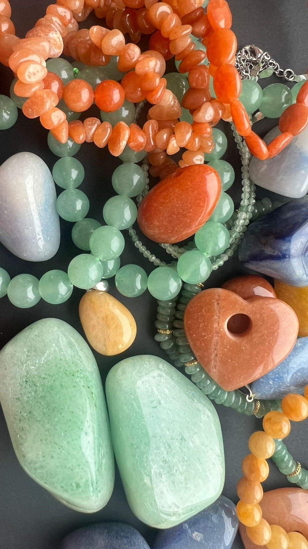 Aventurine crystals in green, yellow and orange hues, mixed with polished stones, bracelets and necklaces, showcasing natural textures and the variety of aventurine gemstones.