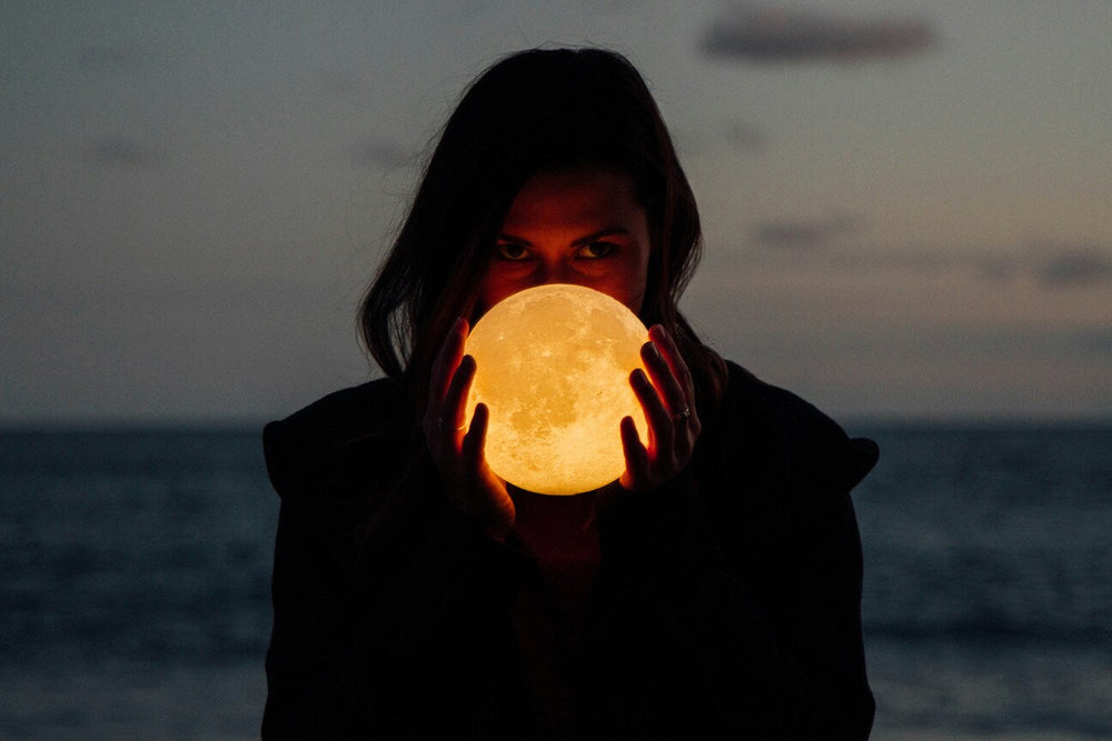 Femeie ținând o lumină în formă de Lună Plină, simbol al intențiilor și energiilor lunare.