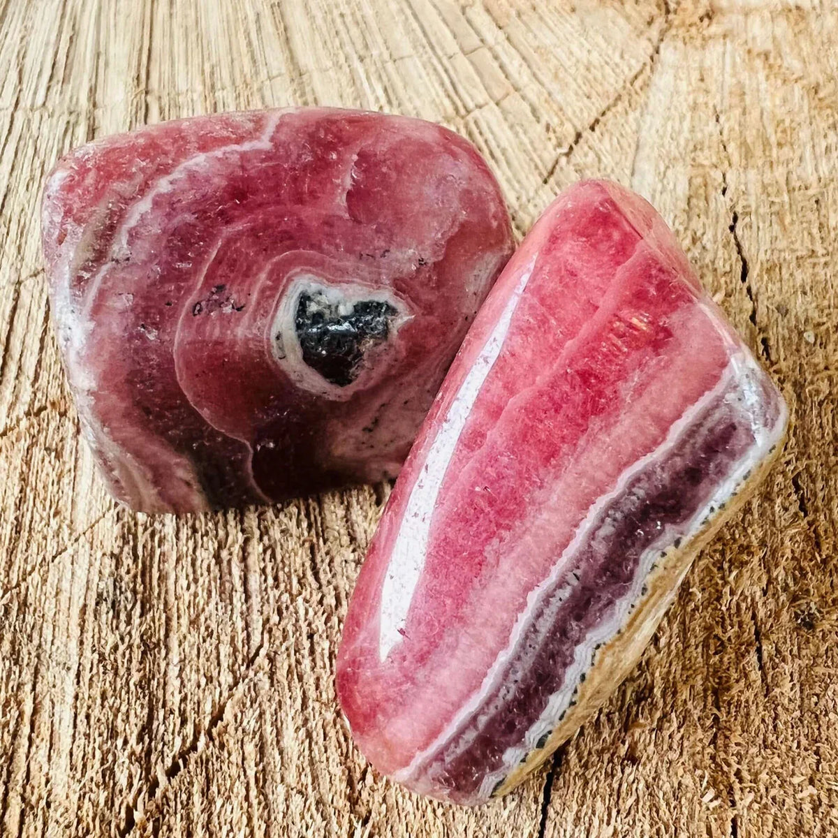 Two polished rhodochrosite tumbled stone. Photo credit: Druzys with natural banding and rich pink hues on wooden background