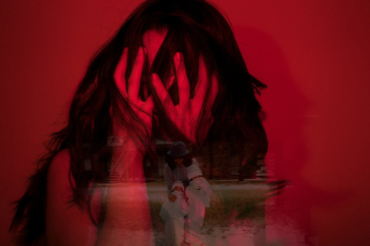 Femeie copleșită de traumă, ascunsă în roșu intens, cu mâinile peste față.